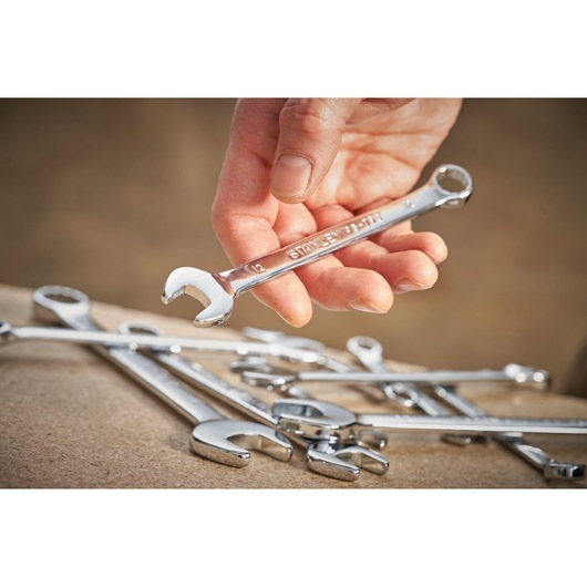 Photo of a hand holding a STANLEY STMT95792-0 combination wrench with other wrenches on a work surface.