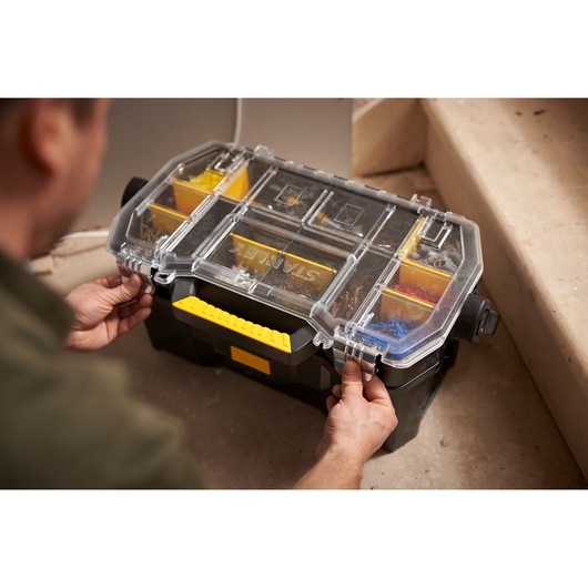 STANLEY STST1-70317 tool organizer with clear lid and yellow handle, being opened by hands on a work site.