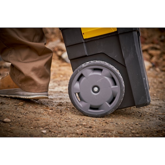 STANLEY STST1-75758 rolling tool box wheel close-up on rough ground, person in brown pants walking nearby.