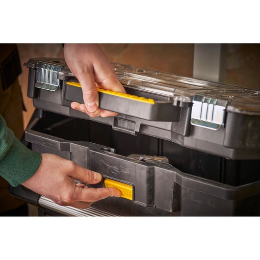 STANLEY STST1-79231 black tool box with yellow handle and latch, close-up showing hands opening.