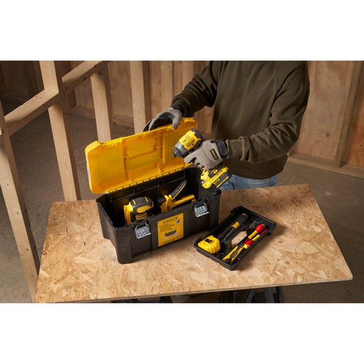 STANLEY STST75787-1 tool box with yellow lid, filled with power tools and accessories on a workbench.