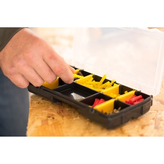 STANLEY STST81679-1 organizer box with yellow and red compartments, hand picking item, top view.