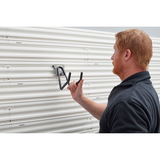 STANLEY STST82608-1 heavy duty wall hook being installed on white slat wall panel, side angle.