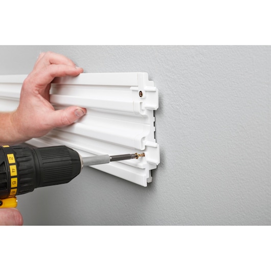 STANLEY STST82610-1 white slatwall being installed with a power drill on a gray wall, close-up angle.