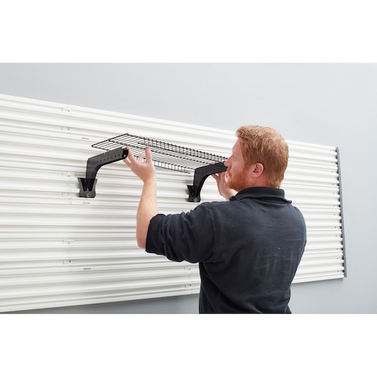 Photo of a person installing a STANLEY STST82613-1 wall-mounted wire shelf on a white panel system.