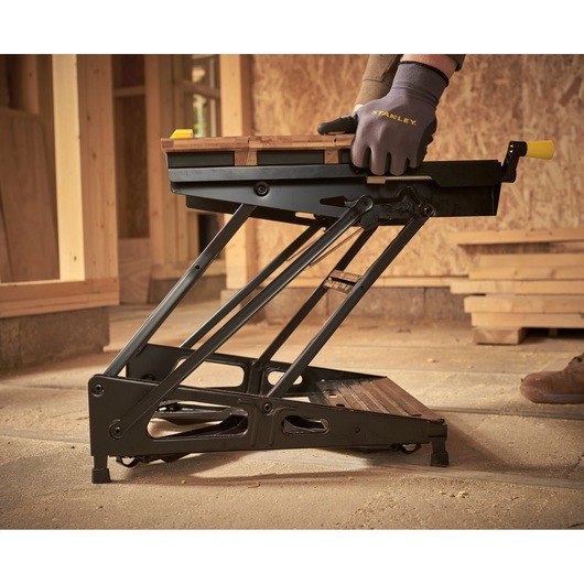 STANLEY STST83400-1 portable workbench with folding metal frame, shown in use on a construction site.