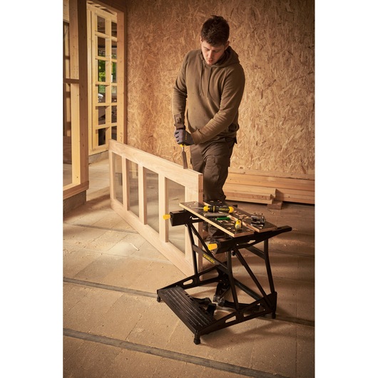 STANLEY STST83400-1 foldable workbench with tools, shown in use in a woodworking workshop.