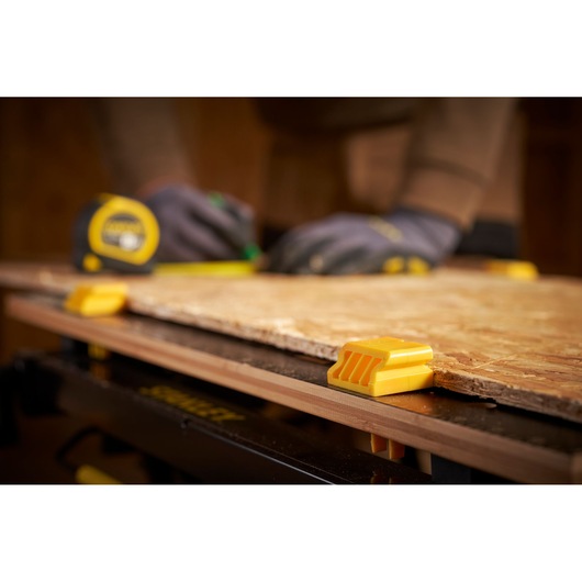 STANLEY STST83800-1 yellow workbench clamp holding wood, close-up, with gloved hands measuring.