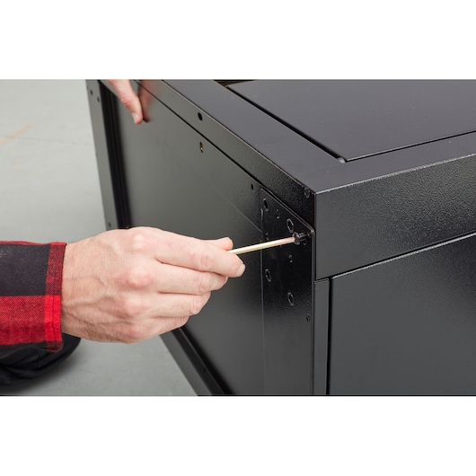 STANLEY STST97595-1 photography of person assembling black metal cabinet with screwdriver, close-up angle.