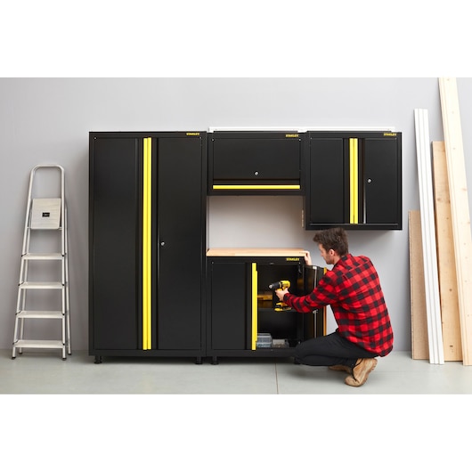STANLEY STST97595-1 black and yellow garage cabinet set, front angle, with person organizing tools.