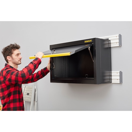 Stanley STST97599-1 wall-mounted storage cabinet with yellow handle opened by person, garage setting.