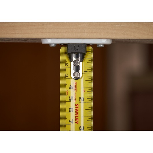 STANLEY XTHT0-33503 tape measure under wood surface, close-up showing yellow blade and measurements.