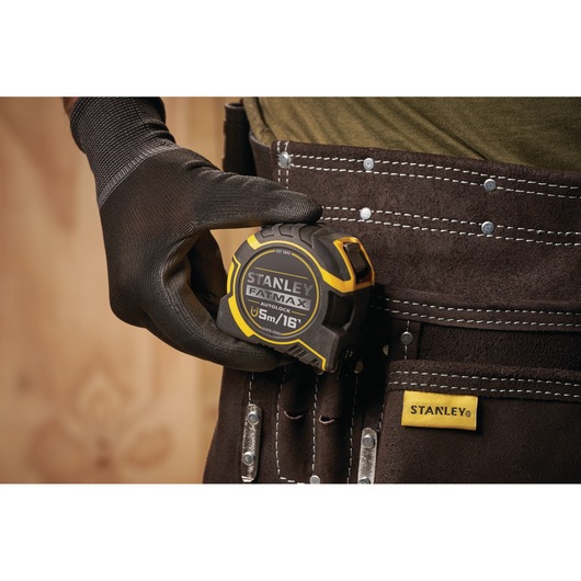 STANLEY XTHT0-33503 tape measure FATMAX 5m, held by gloved hand, tool belt close-up.