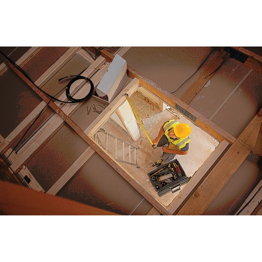 STANLEY XTHT0-33504 tape measure in use by worker in construction setting, viewed from above.