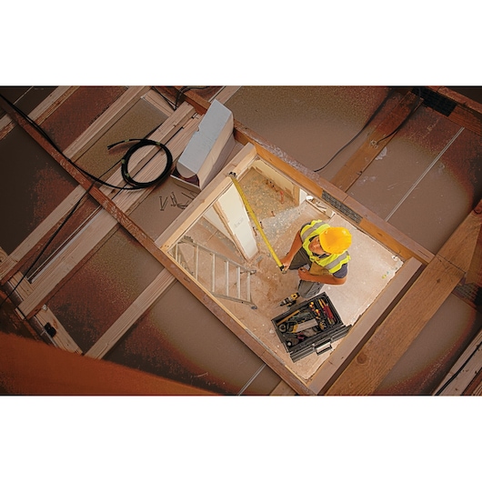 STANLEY XTHT0-33671 tape measure in use by worker in attic, construction scene, overhead angle.